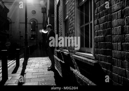 Schwarz-Weiß-Straßenfotografie in London: Mann raucht auf der Straße. Stockfoto