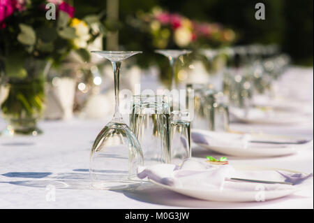 Schöne Dekoration der Tisch mit weißer Tischdecke, Geschirr und Vase mit Blumen. Durchsichtig Gläser, Servietten und Blumensträuße auf der banqu Stockfoto