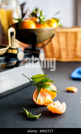 Frische ganze Clementinen mit grünen Blättern in vintage Maßstab und eine geschälte Clementine auf einem Schwarzen Tisch mit einem blauen Tuch und mehrere Gewichte Stockfoto