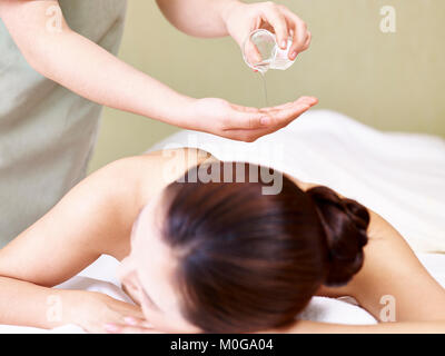 Masseur gießen Öl auf Hand, während Jungen asiatischen liegende Frau auf der Vorderseite auf der Massageliege. Stockfoto