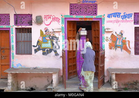 CHITTORGARH, Rajasthan, Indien - Dezember 14, 2017: Eine bunte traditionelles Haus mit Gemälden und eine Frau, die Wasser Topf auf den Kopf Stockfoto