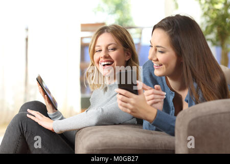 Zwei fröhliche Freunde teilen smart phone Inhalt auf einer Couch im Wohnzimmer zu Hause Stockfoto