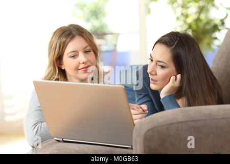 Porträt von zwei Freunden über on-line-Inhalt in einem Laptop auf der Couch zu Hause liegen im Gespräch Stockfoto