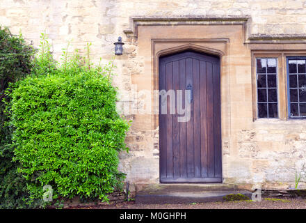 Dunkelbraun Holztüren in einem alten traditionellen Englischen Kalk Steinhaus mit immergrünen Sträuchern auf der Seite. Stockfoto