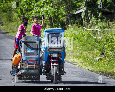 Camalig, Albay, Philippinen. 22 Jan, 2018. Die Menschen fahren mit dem Philippinischen Dreirad Taxi, während sie ihre Gemeinschaften an den Hängen des Mayon Vulkan verlassen. Es gab eine Reihe von Eruptionen auf der Mayon Vulkan in der Nähe von Legazpi Montag. Die Eruptionen begann Sonntag Nacht und weiter durch den Tag. Um ca. 12.00 Uhr den Vulkan gesendet eine Wolke aus Asche und Rauch hoch über Camalig, die größte Gemeinde in der Nähe des Vulkans. Credit: ZUMA Press, Inc./Alamy leben Nachrichten Stockfoto