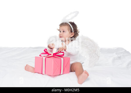 Kleine Engel mit Nimbus sitzen auf dem Bett mit Geschenkboxen, isoliert auf weißem Stockfoto