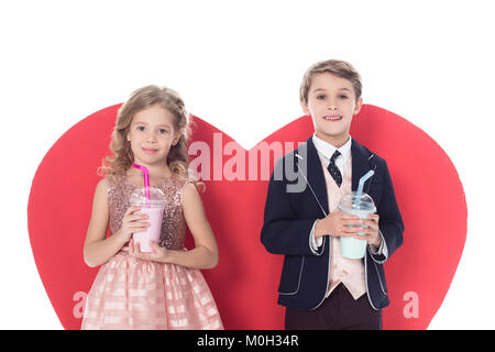 Süße kleine Kinder holding Milchshakes in Plastikbechern und einem grossen roten Herz Symbol hinter auf Weiß isoliert Stockfoto