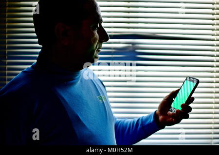 Grüner Bildschirm Bereit Android und mann Betrachtung gegen gestreifte Fenster von Schatten und Licht Muster Stockfoto