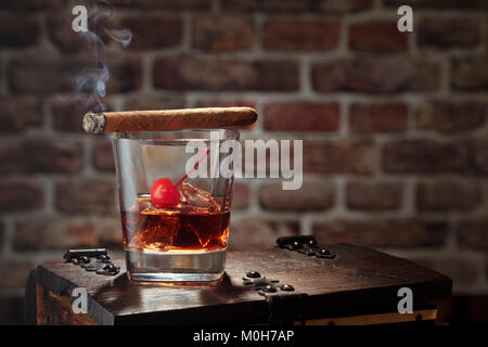 Glas Whiskey mit Rauchen Zigarre und Eiswürfel auf hölzernen Tisch. Stockfoto