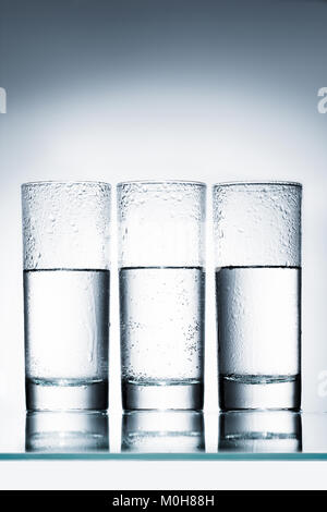 Halb voll Gläser Wasser in der Zeile auf eine reflektierende Oberfläche zu richten. Stockfoto