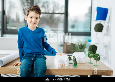 Fröhliche Junge sitzt am Tisch und berühren Haus Modell Stockfoto