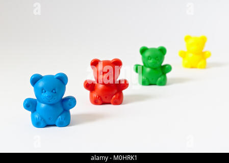 Kunststoff Teddybären auf Weiß in verschiedenen Farben (Blau, Rot, Grün, Gelb) bilden eine Linie, die in den Hintergrund verschwindet, isoliert Stockfoto