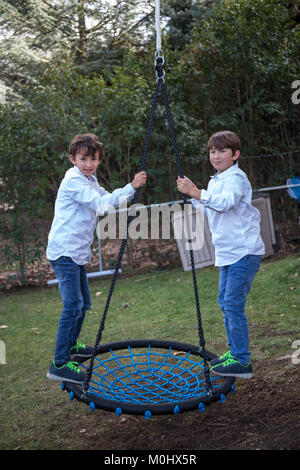 Jüngere Geschwister spielen im Hinterhof auf der Schaukel Stockfoto