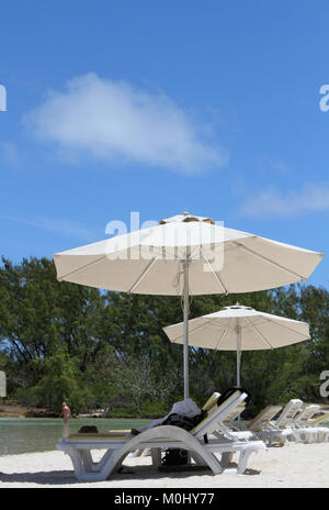 Sonnenschirme und Liegen am Strand in der Nähe von Forest Patch auf der Ile aux Cerfs, einer privaten Insel in der Nähe der Ostküste der Republik Mauritius in Stockfoto