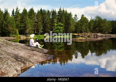 Ein kleiner Junge sitzt und Angeln auf einem malerischen Rocky See in Norwegen an einem Sommertag. Stockfoto