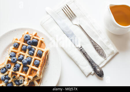Blick von oben auf die Teller köstliche Waffeln mit Blaubeeren, Honig und Besteck Stockfoto