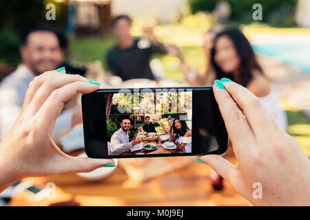 Junge Menschen, die Spaß im Freien. Gruppe von Freunden posiert, während ihre Freundin ein Foto mit seinem Smart Phone. Weibliche Hände unter Bild der frien Stockfoto