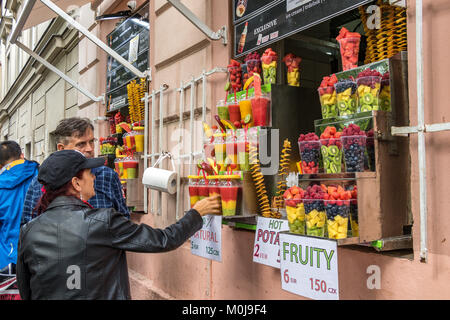 Frau Kauf eines Fruit Smoothie aus einem Loch in der Wand Kiosk mit Wannen von frischem Obst und Gemüse Smoothies auf Anzeige Stockfoto