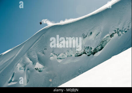 Eine professionelle, Freeriden Snowboarder, dreht sich in der Luft auf einem schneebedeckten Hang vor blauem Himmel, British Columbia, Kanada Stockfoto