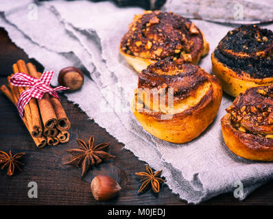 Süße Brötchen mit Zimt und Nüsse auf einem grauen Serviette neben Zimtstangen und Sternanis Stockfoto