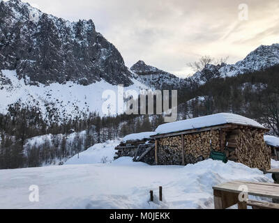 Val Maira, Piemont - Italien; verschneite Berglandschaft mit Stapel von Brennholz Stockfoto