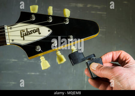 Gibson Flying V E-Gitarre Spindelstock, mit den Fingern ein Mann hält eine Saitenkurbel gegen ein Tuning peg/Tuner, einen String zu lösen oder festziehen. Stockfoto