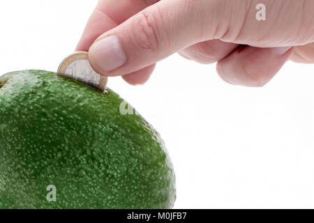 Avocados als Sparschwein, in dem die Hand eine Münze. Stockfoto