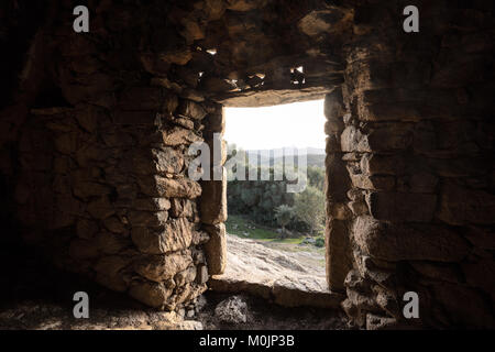 Blick auf Olivenbäume und der Berge durch den Eingang zu einem alten Stein Höhlenwohnung in die Felsen am Ostriconi in Korsika gebaut gesehen Stockfoto