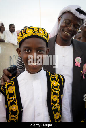 Kind in traditioneller Anzug & kufi für die mawlid Festival, feiert mit seinem Vater und Bruder, die in der überfüllten Corniche von Lamu Island, Kenia Stockfoto