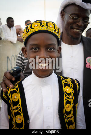 Kind in traditioneller Anzug & kufi für die mawlid Festival, feiert mit seinem Vater und Bruder, die in der überfüllten Corniche von Lamu Island, Kenia Stockfoto