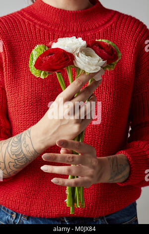 Mädchen mit einem Tattoo auf ihre Hände in einem roten Strickpullover hält einen Blumenstrauß. Ein Happy Valentinstag Stockfoto