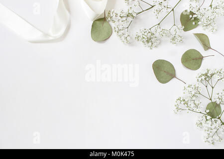 Styled Foto. Feminine Hochzeit desktop Mockup mit Baby's Atem Gypsophila Blumen, trockenen grünen Eukalyptus Blätter, Satinband und weißen Hintergrund. Der leere Raum. Ansicht von oben. Bild für Blog. Stockfoto