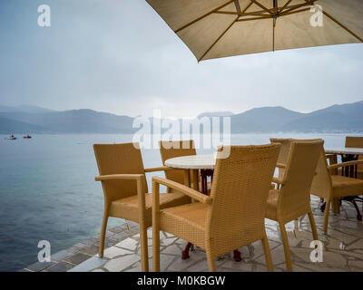 Tische und Stühle unter einem Sonnenschirm an der Küste der Bucht von Kotor; Bjelila, Opstina Tivat, Montenegro Stockfoto