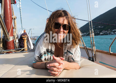 Eine Frau legt auf ein Deck ein Segelboot mit windswept Haare in die Kamera schaut an der Küste von Montenegro Montenegro Stockfoto