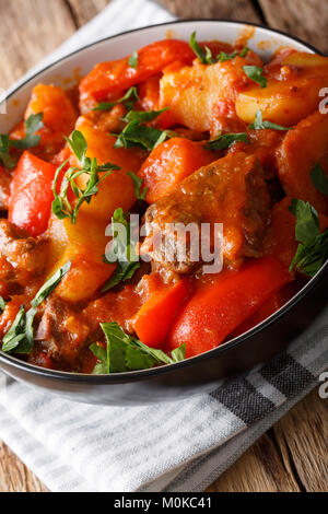 Langsam gekochtes Rindfleisch mit Kartoffeln, Tomaten, Paprika, Karotten und Zwiebeln in der Nähe in einer Schüssel auf dem Tisch. Vertikale Stockfoto