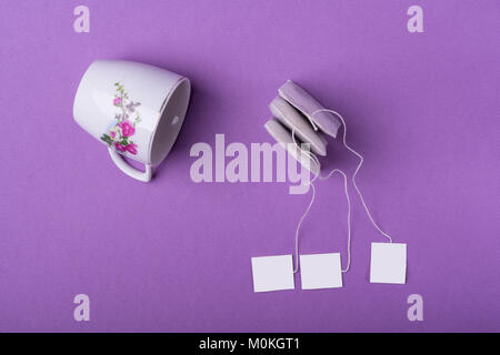 Dekor Porzellan weiße Tasse mit drei Teebeutel auf lila Hintergrund. top View Studio shot Stockfoto