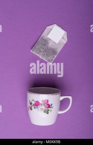 Single Porzellan weiße Tasse mit einem Teebeutel auf lila Hintergrund. top View Studio shot Stockfoto