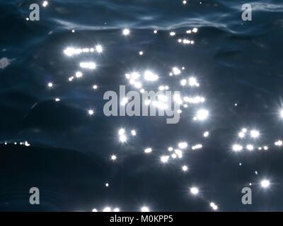 Sterne im dunklen Wasser. Unscharf bokeh Hintergrund des blauen Wassers mit Sun Reflexionen Stockfoto