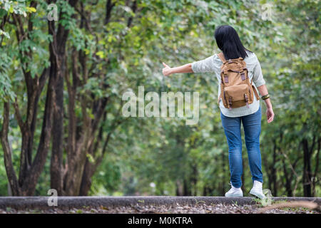 Asiatische Frau Backpacker auf Landstraße mit Baum im Frühjahr saisonale, allein reisen oder Alleinreisende Konzept. Stockfoto