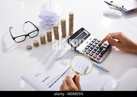 Der Unternehmer Hand Analyse von Rechnungen mit Lupe Vor gestapelte Münzen Grafik Stockfoto