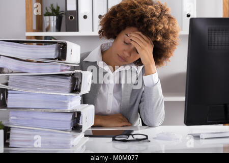 Stressvolle Afro-amerikanische Geschäftsfrau im Büro mit Stapeln von Dateien Stockfoto