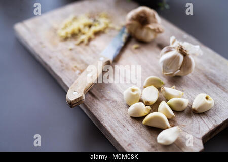 Knoblauch und Messer auf einer hölzernen Schneidebrett. Stockfoto