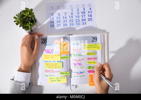 Ansicht der Geschäftsfrau, die Hand mit dem Kalender Schreiben Zeitplan im Tagebuch auf dem Schreibtisch im Büro Stockfoto