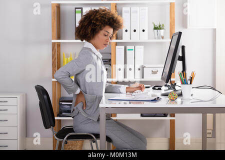 Junge Geschäftsfrau mit Rückenbeschwerden bei der Arbeit im Büro Stockfoto