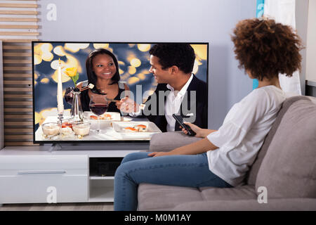 Frau sitzt auf einem Sofa vor dem Fernseher zu Hause Stockfoto