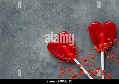 Zwei rote Herzen Form Süßigkeiten Lutscher auf Sticks Blumen auf dunklem Stein Hintergrund. Valentine romantische Liebe Grusskarten Banner Poster mit Platz kopieren. C Stockfoto