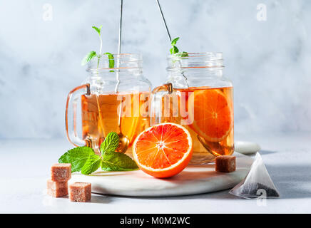 Traditionelle Eistee mit Orange und Minze und Eis in Maurergläser. Erfrischende Sommer Drink auf weißem Marmor board Stockfoto