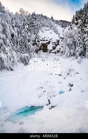 Kleine türkis Creek fließt durch Schnee verdeckte Winterlandschaft mit Wald im Hintergrund Stockfoto