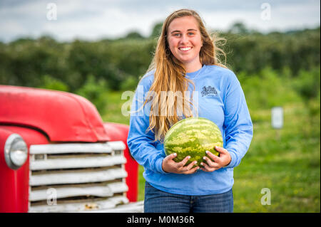 Junge lächelnde Frau wirft Holding Wassermelone in ihren Armen mit Oldtimer im Hintergrund, Salisbury, Maryland Stockfoto