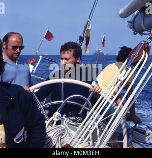 AJAX-NEWS FOTOS. 1977. Irische See. - FASTNET RACE SKIPPER - ROBIN KNOX - Johnston (GB) AM RAD DER BOGENSCHÜTZEN 77 YACHT CONDOR WÄHREND DES FASTNET RACE, dem IKONISCHEN LEUCHTTURM ACHTERAUS. Yachteigner Bob BELL AUF DER LINKEN SEITE. Foto: Jonathan Eastland/AJAX REF: 703734 14 Stockfoto